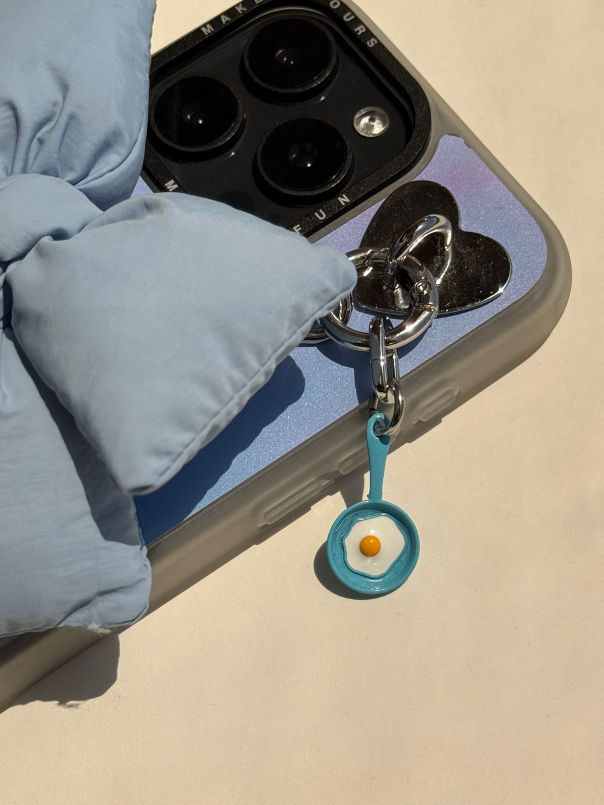 Un charm y accesorio colgante Blue Sunny Side Up Charmie en color azul sujeto a un celular - Build A Caze
