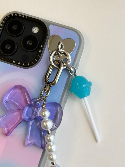Un charm y accesorio colgante Blueberry Pop Charmie en color azul sujeto a un celular - Build A Caze