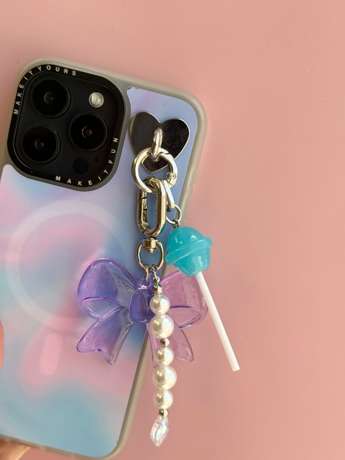 Un charm y accesorio colgante Blueberry Pop Charmie en color azul y morado sujeto a un celular - Build A Caze