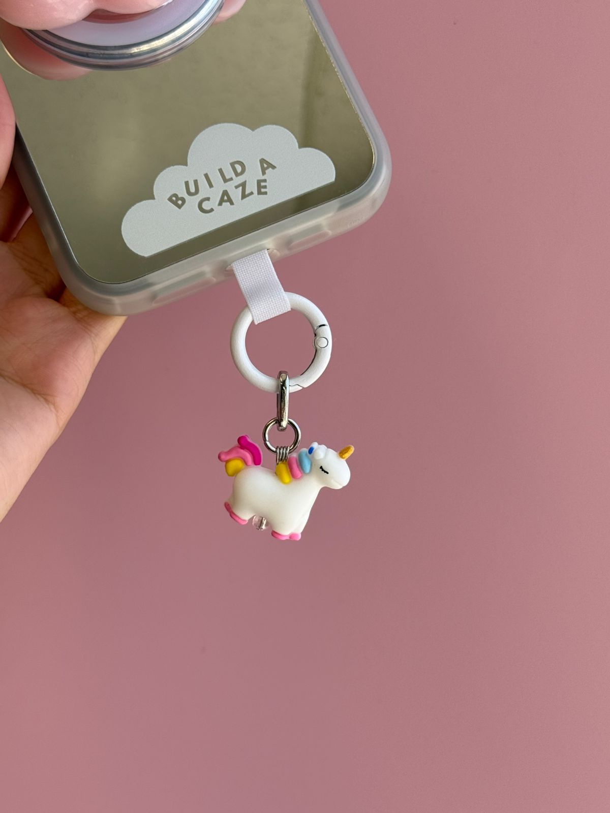 Un charm y accesorio colgante Candy Uni Spark Charmie en color lila y rosa sujeto a un celular - Build A Caze