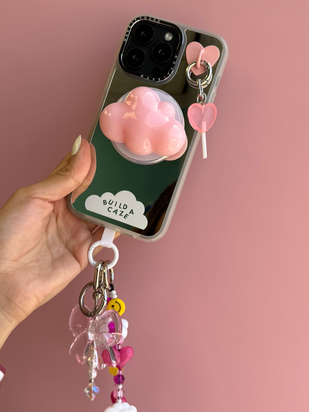Un charm y accesorio colgante Coral Pink Lollie Pop Charmie en color rosa sujeto a un celular - Build A Caze