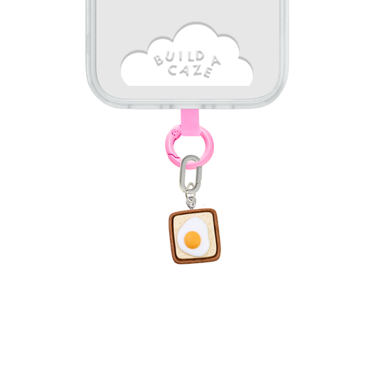 Un charm y accesorio colgante Eggie Toast Bites Charmie en color marrón y blanco sujeto a un celular - Build A Caze