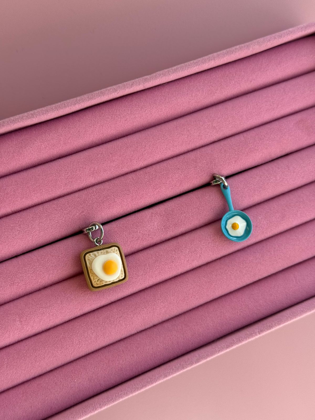 Un charm y accesorio colgante Eggie Toast Bites Charmie en color marrón y blanco sujeto a un celular - Build A Caze