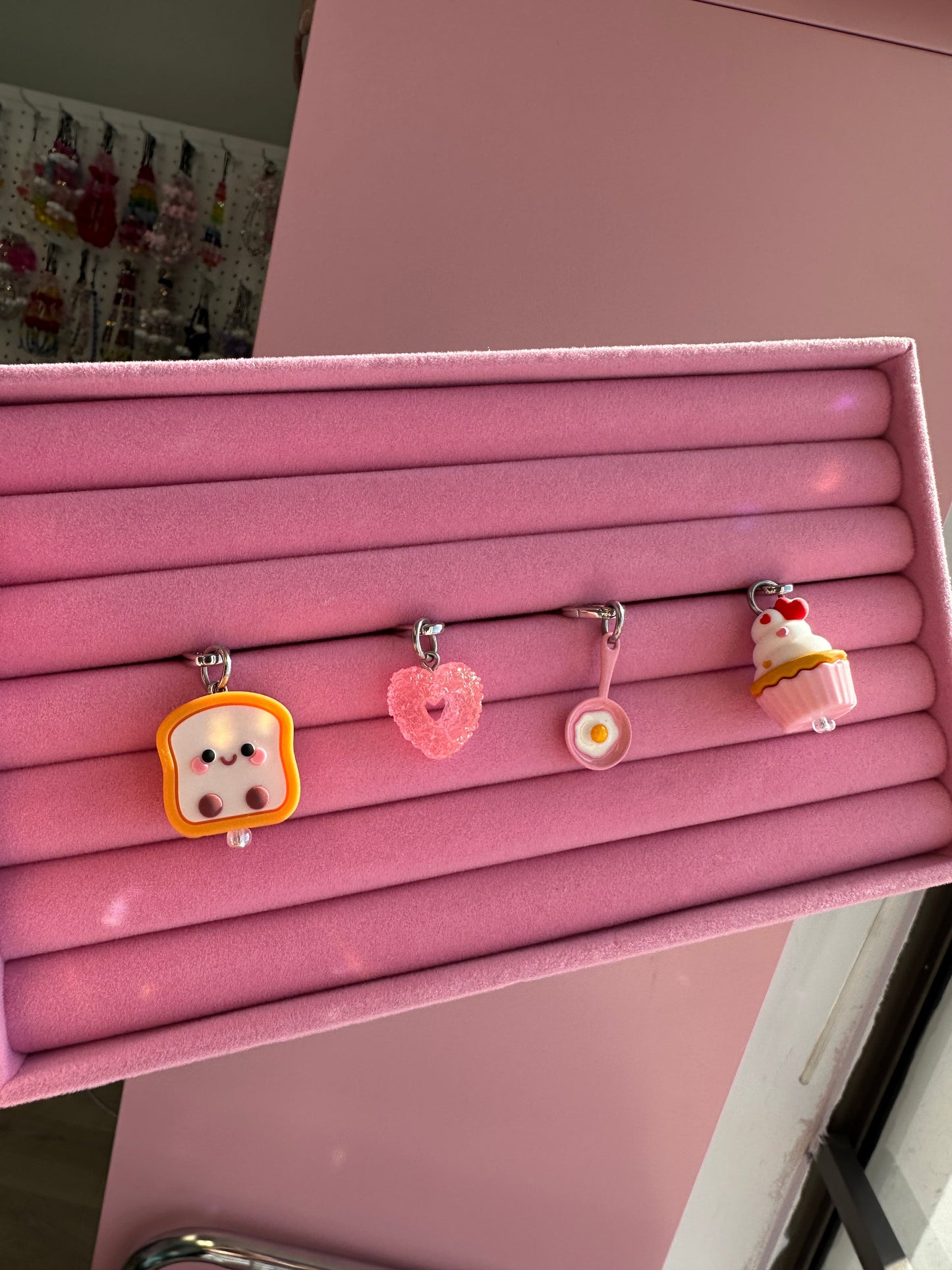 Charmie Sunny Side Up rosa exhibido en un estante rosa junto a charmie de corazón