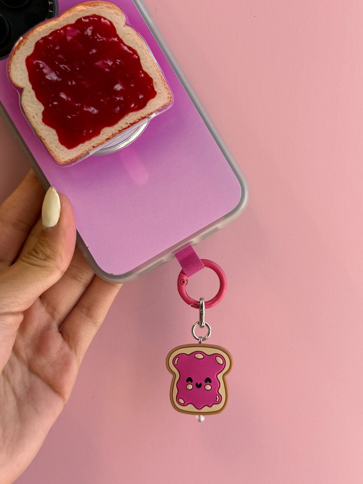 Un charm y accesorio colgante Jammy Toastie Charmie en color marrón y rosa sujeto a un celular - Build A Caze