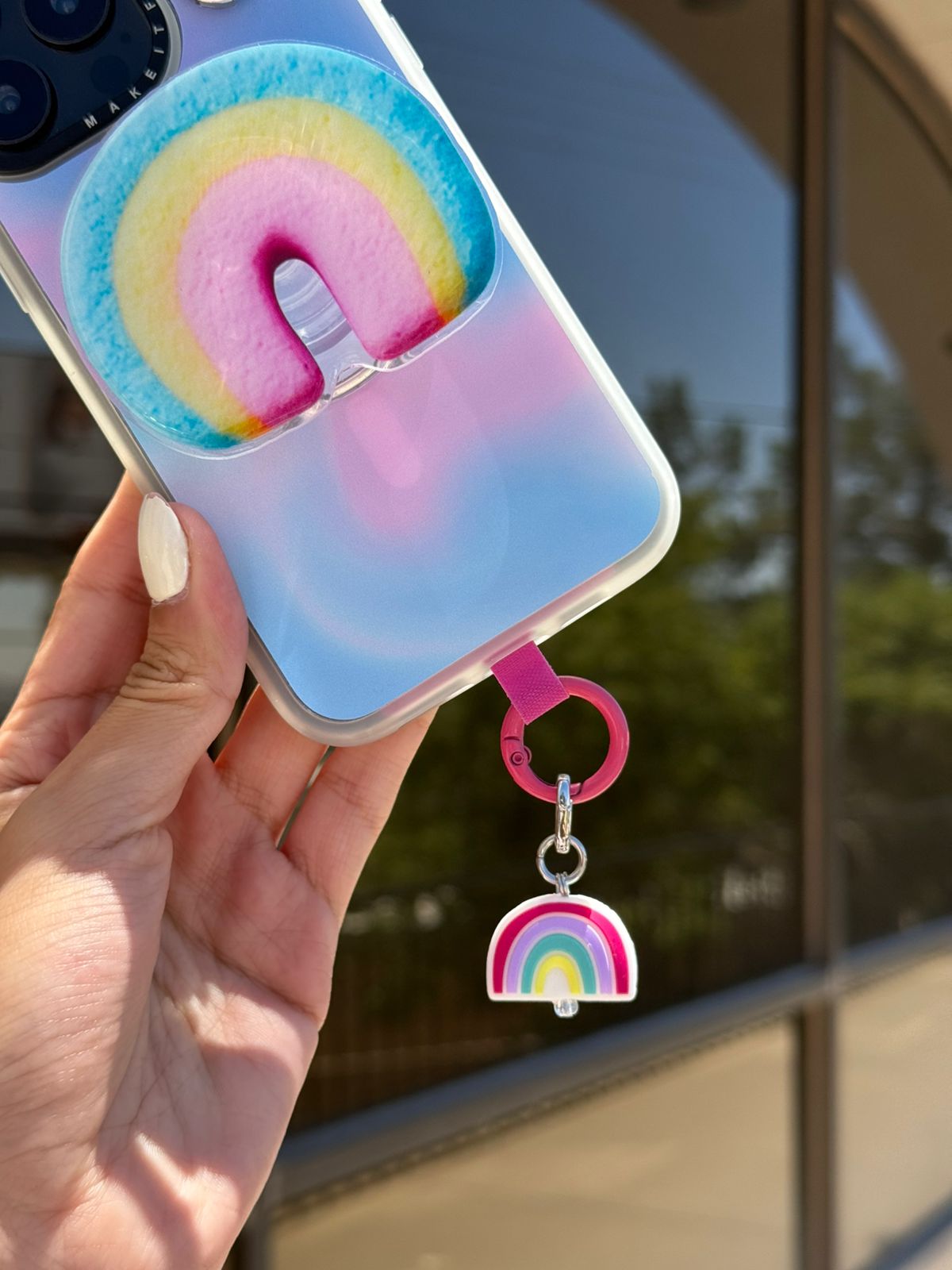 Un charm y accesorio colgante Rainbow Dreamie Charmie en colores pastel arcoíris sujeto a un celular - Build A Caze