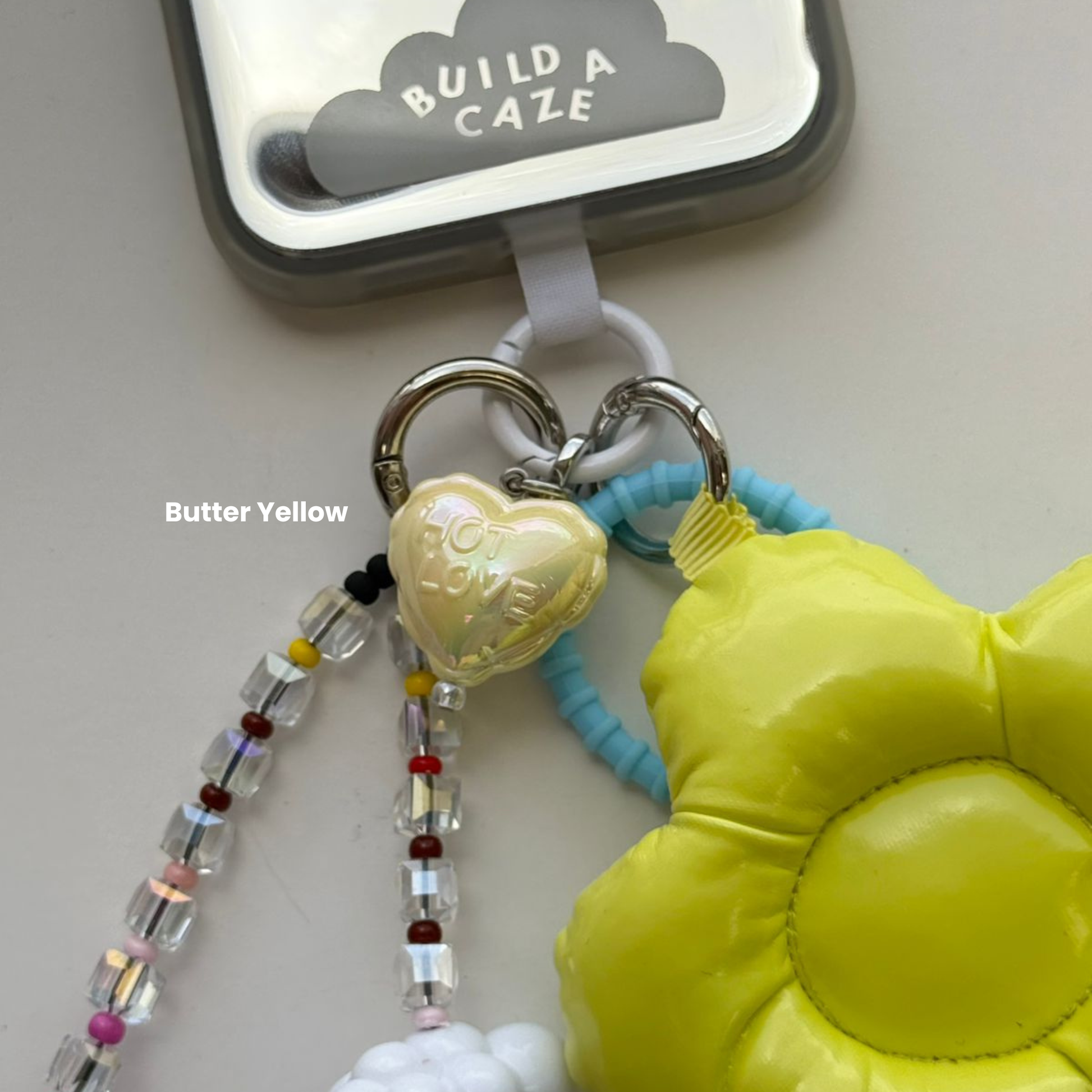 Un charm aqua con forma de globo de corazón sujeto a un celular como accesorio colgante - Build A Caze.