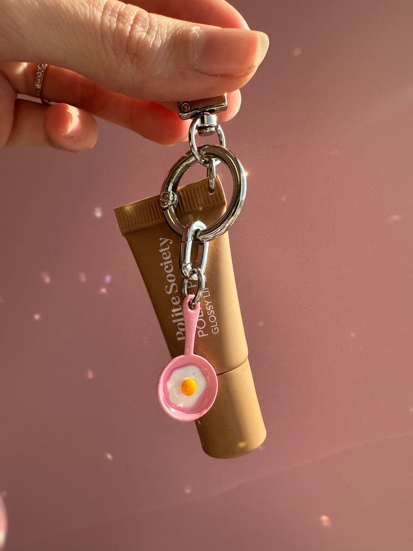 Mano sosteniendo un labial con el Charm Sunny Side Up rosa enganchado al llavero