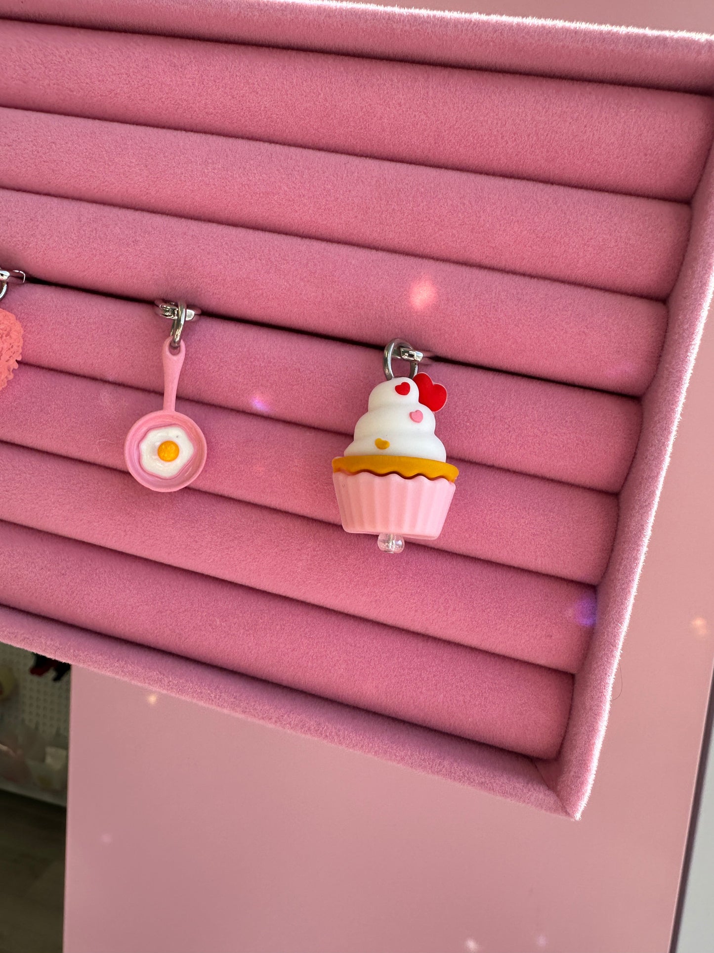 Sunny Side Up rosa exhibido en un estante rosa junto a un charm en forma de cupcake Build A Caze